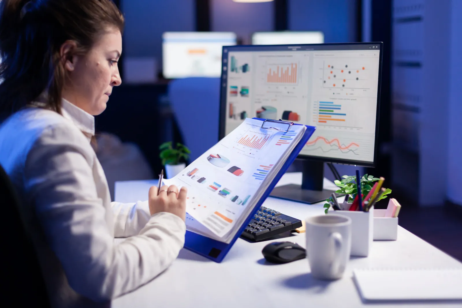 Woman comparing charts on a clipboard with data on her computer